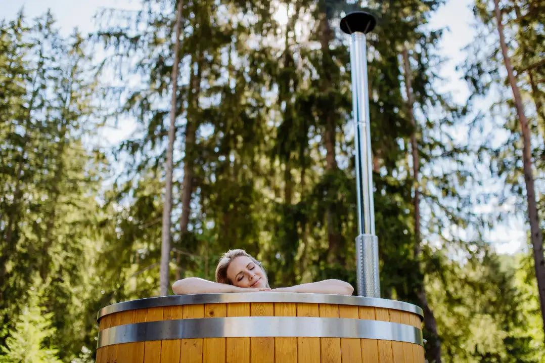 Frau entspannt in einem holzbefeuerten Hot Tub aus Holz im Garten mit Edelstahlkamin