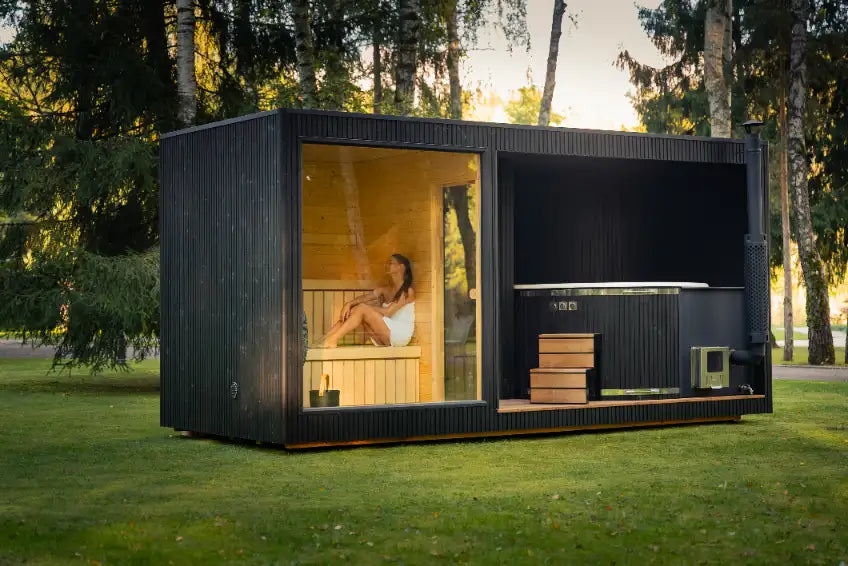 Moderne schwarze Outdoor-Sauna mit großer Panorama-Glasfront und beleuchtetem Innenraum im Garten