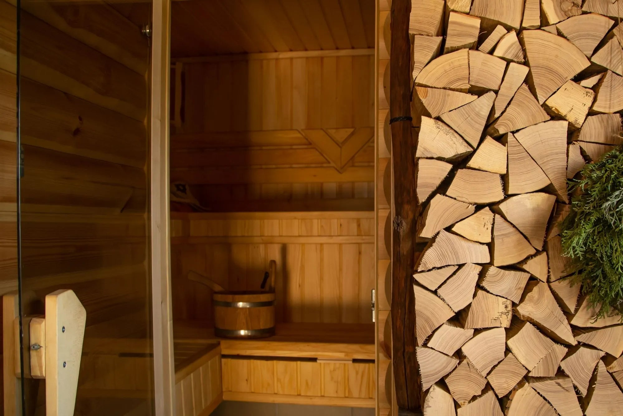 Detailansicht einer modernen Sauna mit warmer Holzverkleidung und gestapeltem Brennholz – hochwertige Verarbeitung und natürliche Materialien für stilvolle Wellnessmomente.