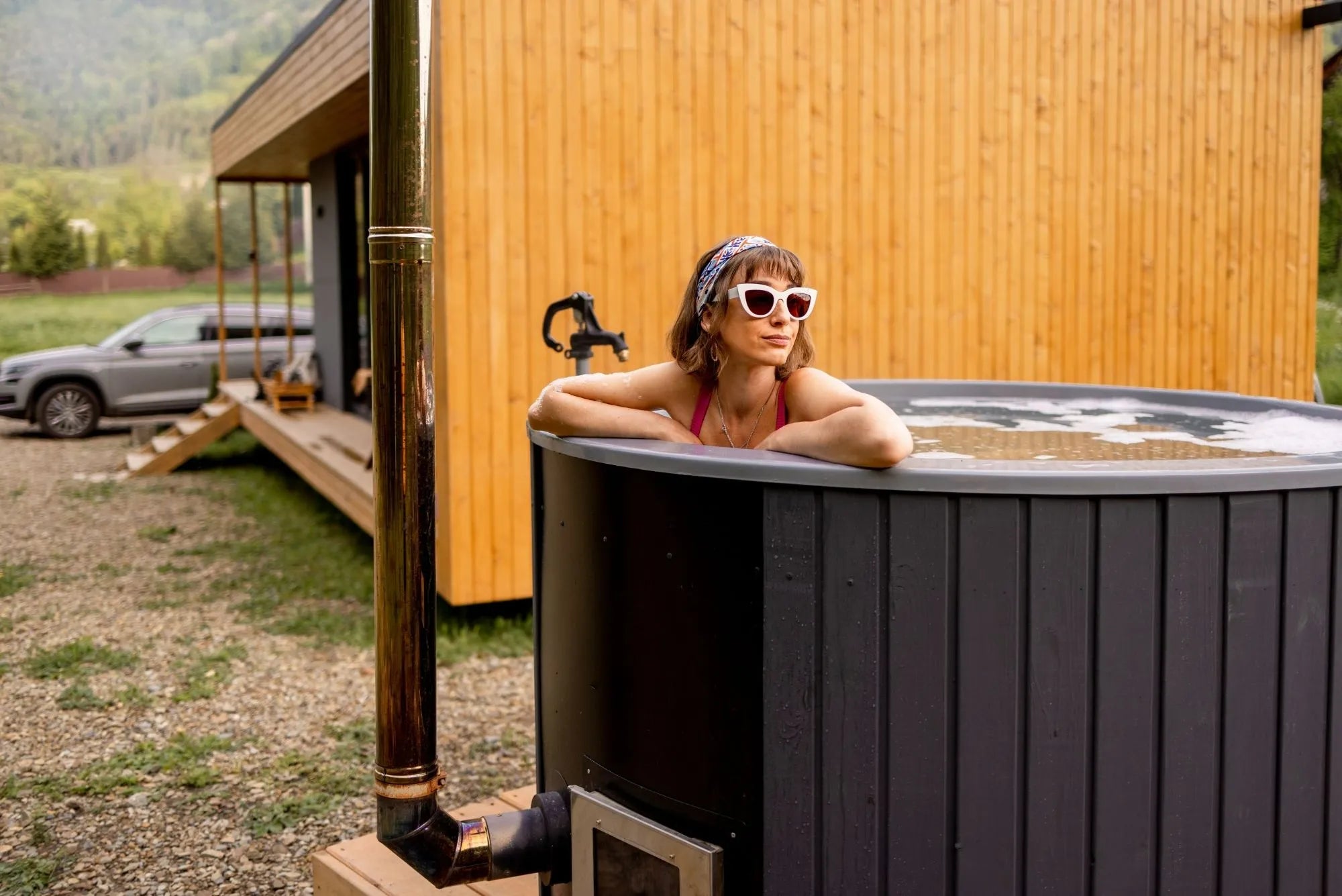 Outdoor hot tub mit holzofen neben modernem Haus – badefass mit holzofen als Alternative zur whirlpool badewanne 2 personen oder holzbadewanne für den Garten.