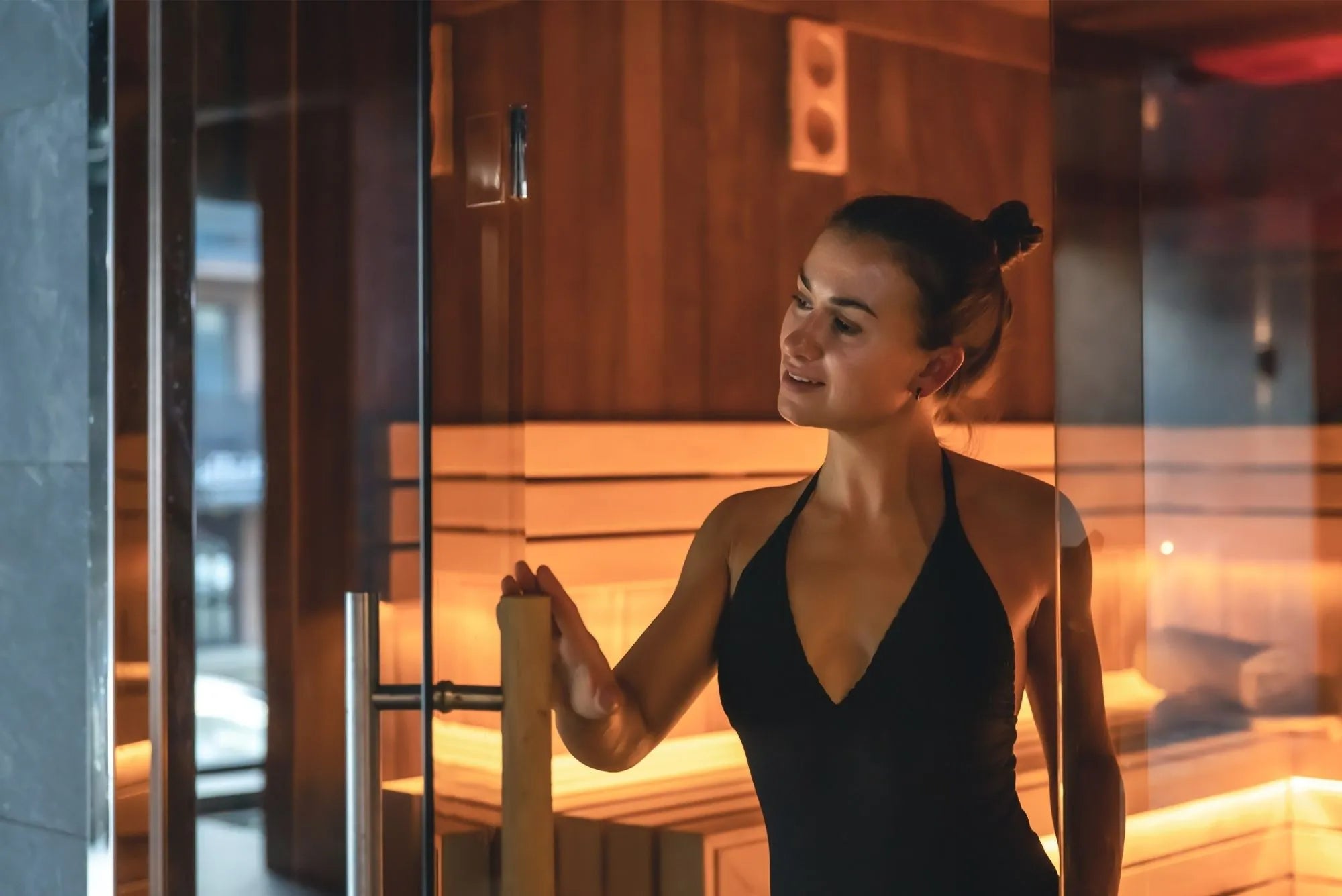 Frau in moderner sauna innen mit hochwertiger sauna holzart, LED-Beleuchtung und Glasfront – finnische sauna aus holz für sauna im Haus oder als großzügige Saunen Lösung.