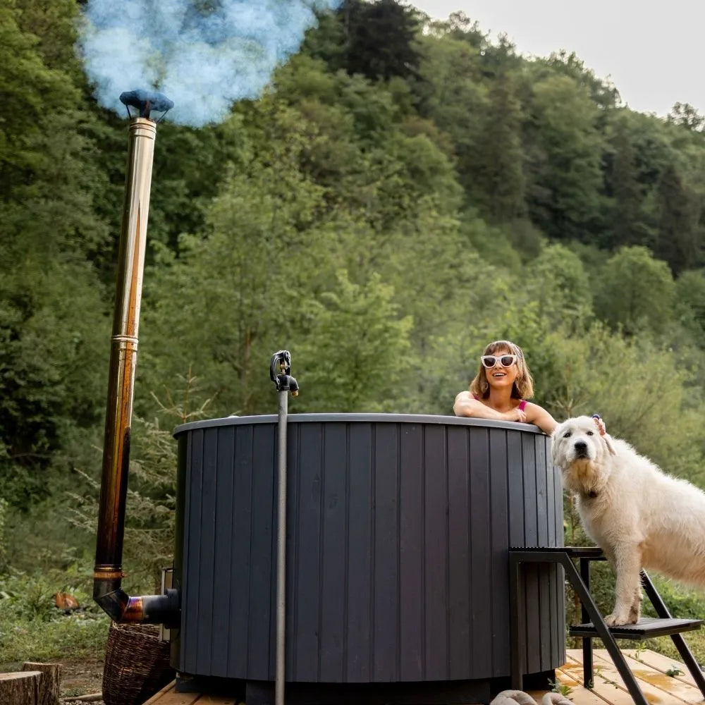 Frau im schwarzen Hot Tub im Grünen, daneben ein Hund auf einer kleinen Treppe.