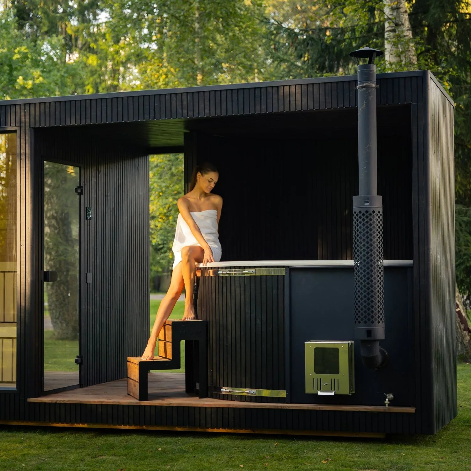 Großzügige Design-Sauna Taurus Grand mit angeschlossenem Hot Tub und Holzofen im Garten – exklusive Kombination aus Sauna und Whirlpool für ganzheitliche Wellness im Freien.